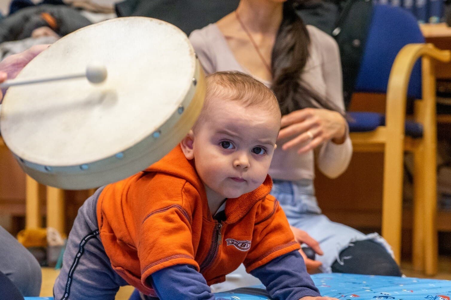 Baby sitzt vor einer Rahmentrommel und greift nach den Schlägeln
