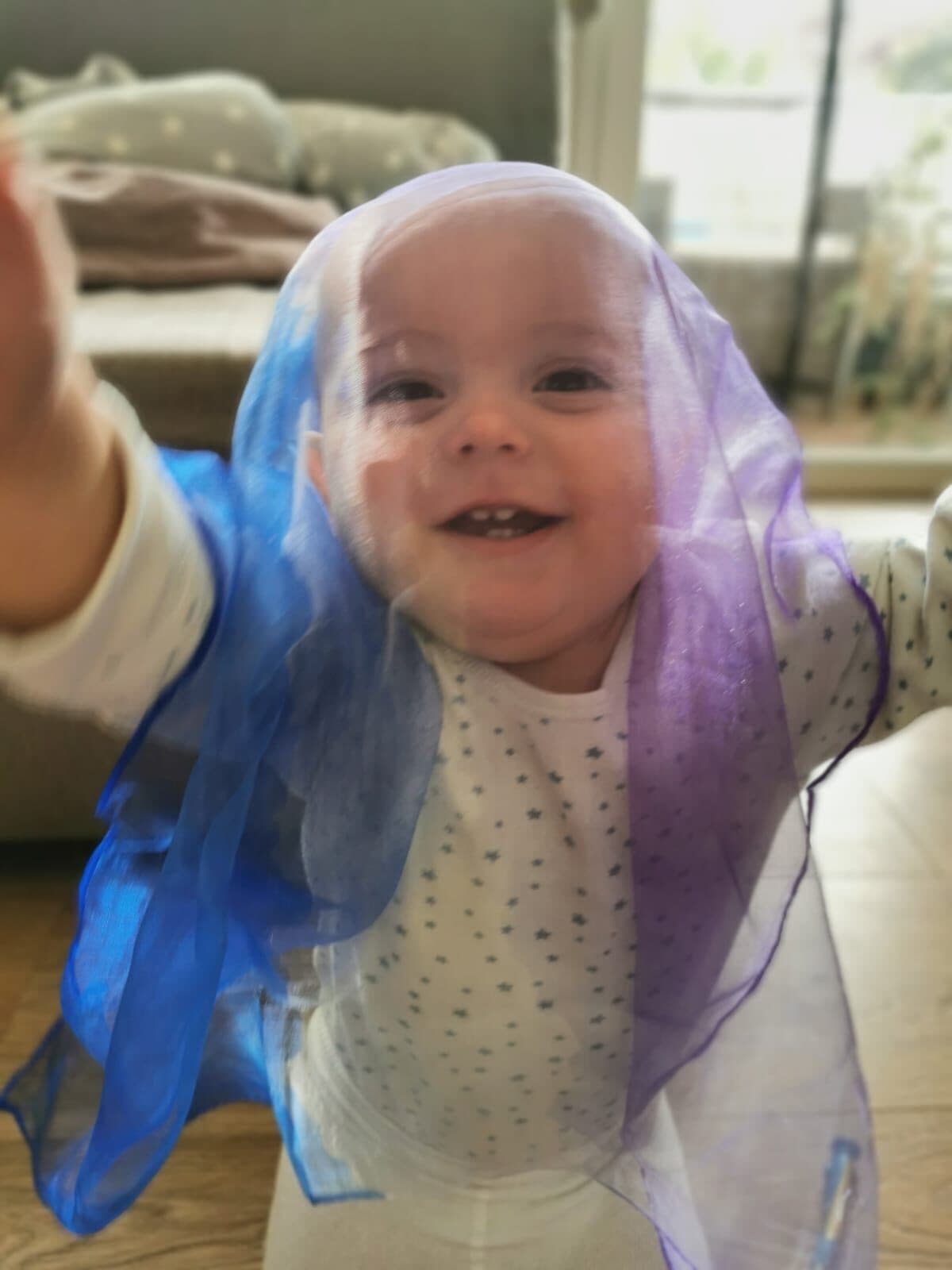 Lachendes Baby mit einem lila Schwungtuch über dem Kopf