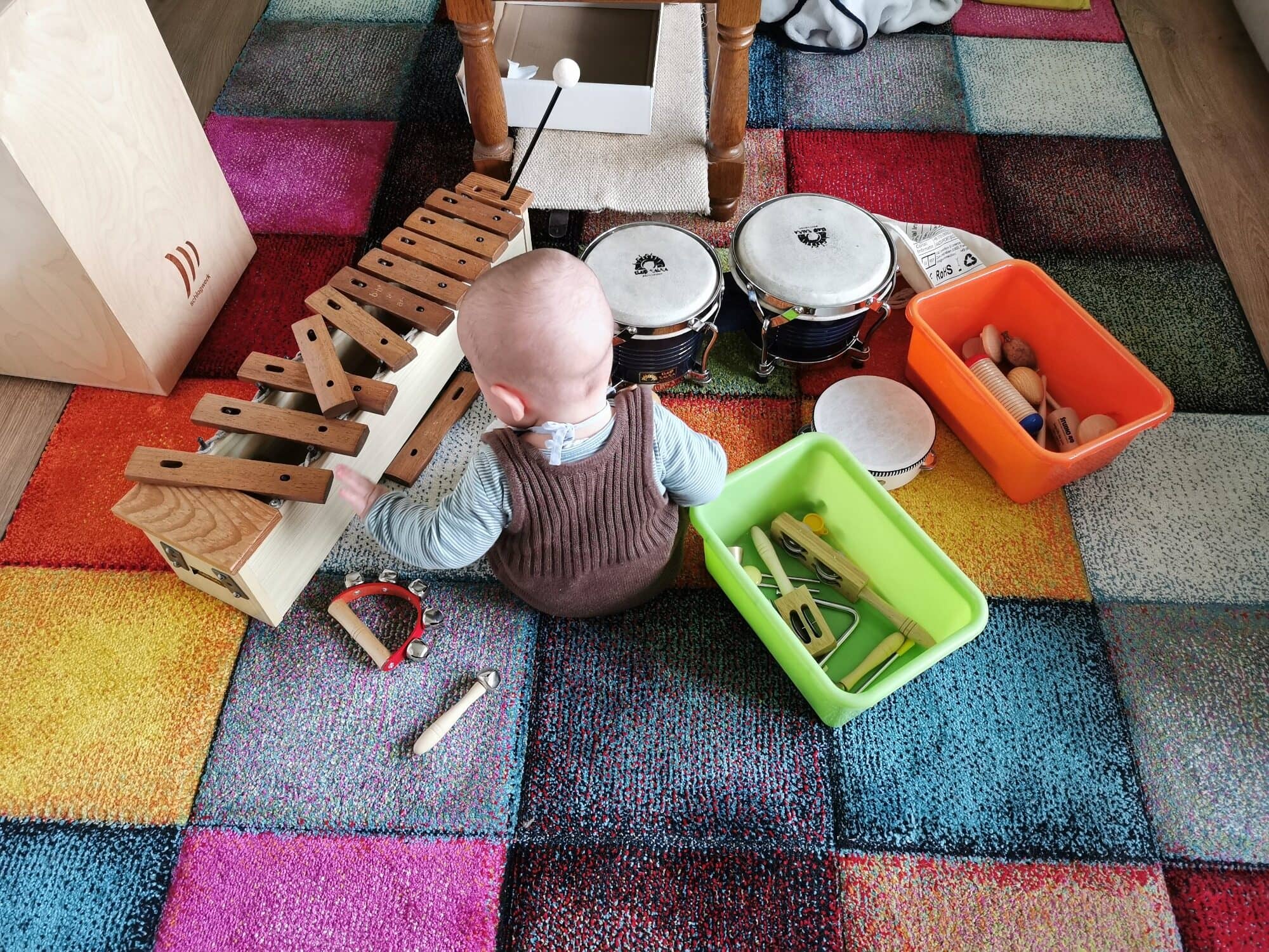 Baby sitzt vor Xylophon und Bongos und greift nach den Schlägeln